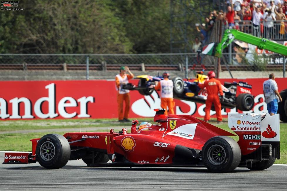 Fernando Alonso (Ferrari) jubelt, während im Bildhintergrund das Auto von Sebastian Vettel (Red Bull) geborgen wird.