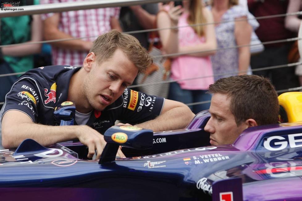 Sebastian Vettel (Red Bull) erklärt WRC-Star Sebastien Ogier (Volkswagen) seinen Arbeitsplatz