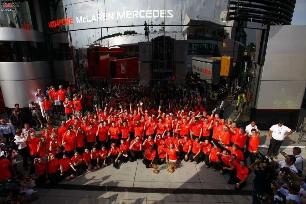 McLaren bejubelt den Sieg in den traditionellen orangefarbenen T-Shirts. Im Hintergrund: das imposante Communications-Centre.