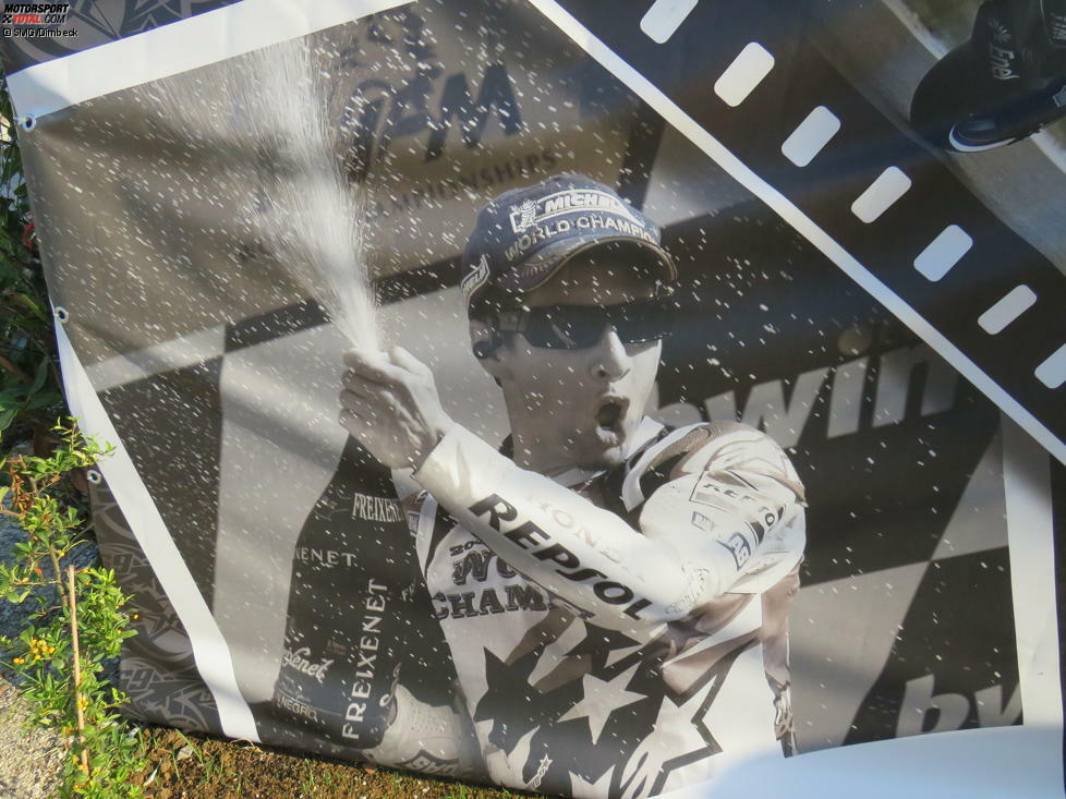 Gesäumt wird die Gedenkstätte von einer Fotocollage mit zahlreichen Abbildungen in schwarz/weiß aus Haydens erfolgreicher Karriere als Motorradrennfahrer.