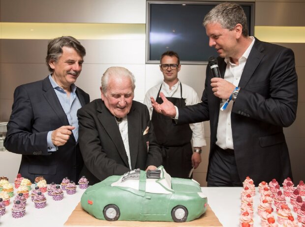 44. AvD Oldtimer Grand-Prix: Renn- und Testfahrerlegende Norman Dewis schneidet seine Geburtstagstorte zum 96. an. Links Jaguar Land Rover-Chef Dr. Rolf Speth, rechts Deutschland-Chef Peter Modelhart.