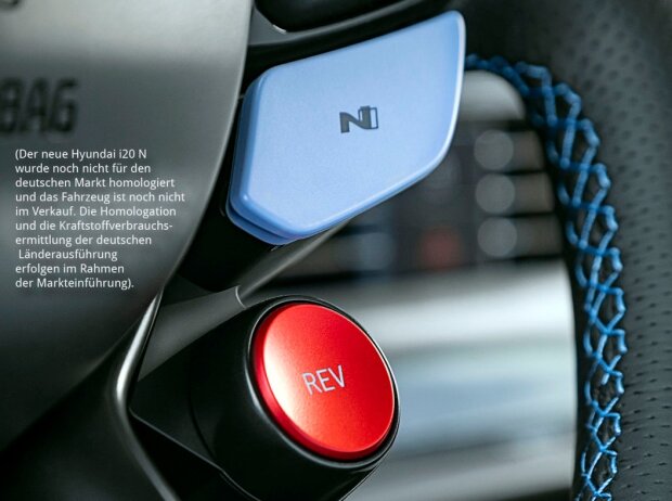 Das Lederlenkrad des Hyundai i20 N 2020 von schräg rechts unten mit blauen Ziernähte am Lenkradkranz, links davon ein großer runder roter Knopf mit der Aufschrift 