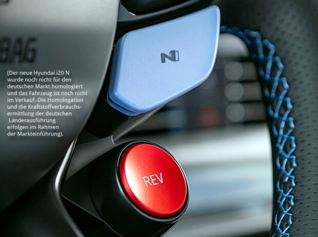 Das Lederlenkrad des Hyundai i20 N 2020 von schräg rechts unten mit blauen Ziernähte am Lenkradkranz, links davon ein großer runder roter Knopf mit der Aufschrift Das Lederlenkrad des Hyundai i20 N 2020 von schräg rechts unten mit blauen Ziernähte am Lenkradkranz, links davon ein großer runder roter Knopf mit der Aufschrift