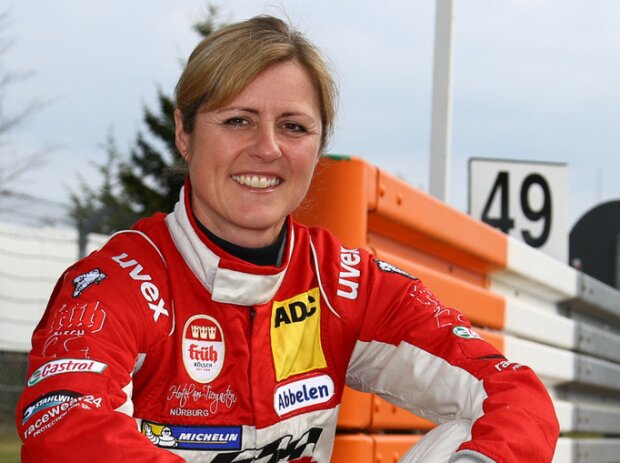 Titel-Bild zur News: Sabine Schmitz posiert auf einem Randstein der Nürburgring-Nordschleife