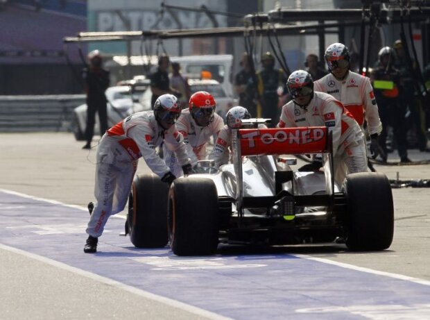 Mechaniker schieben den McLaren von Jenson Button zurück nach einem fehlerhaften Boxenstopp beim Formel-1-Rennen in China 2013