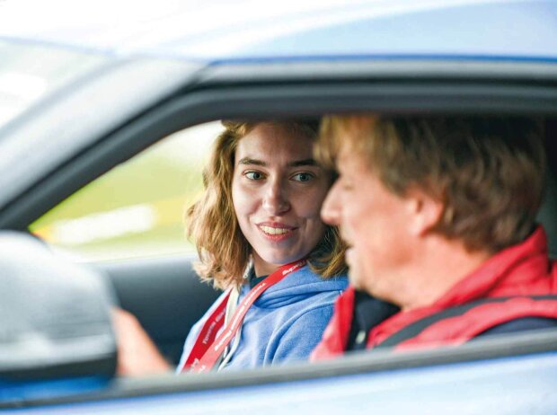 Seitlicher Blick in ein Auto. Eine Frau sitz auf dem Beifahrersitz eines Autos und schaut einen Mann an, der auf dem Fahrersitz sitzend etwas erklärt.