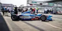 Ein blau-weißer Benetton Formel-1-Rennwagen ist von der Seite zu sehen, wie er seine Garage verlässt und in die Boxengasse einbiegt.