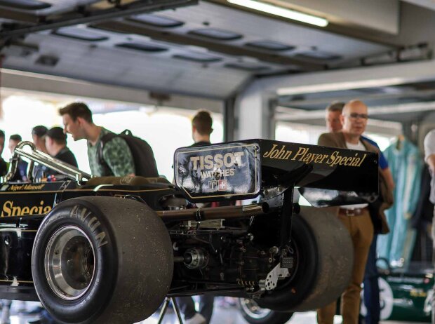 Das Heck eines aufgebockten schwarz-goldenen Formel-1-Autos aus den 1980ern wird in der Garage von Fans bestaunt