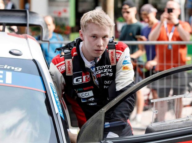 Kalle Rovanperä steht hinter der geöffneten Fahrertür seines Rallye-Autos und blickt in die Kamera