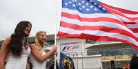 Zwei Frauen posieren mit der US-Flagge in der Formel-1-Startaufstellung