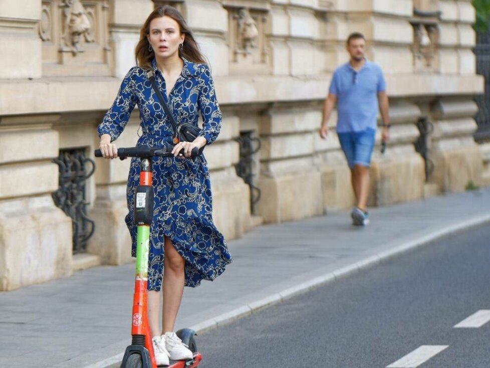 E-Scooter Versicherung: Junge Frau in blauem Kleid fährt E-Scooter auf der Straße
