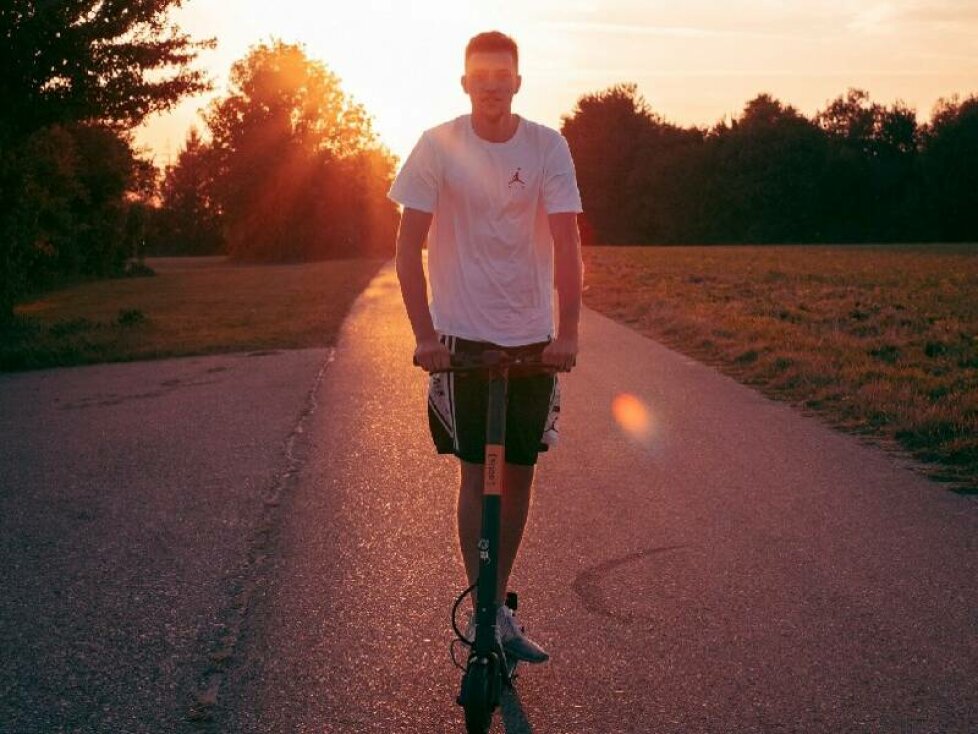 E-Scooter Versicherung: Junger Mann fährt E-Scooter auf einem Feldweg bei Sonnenuntergang